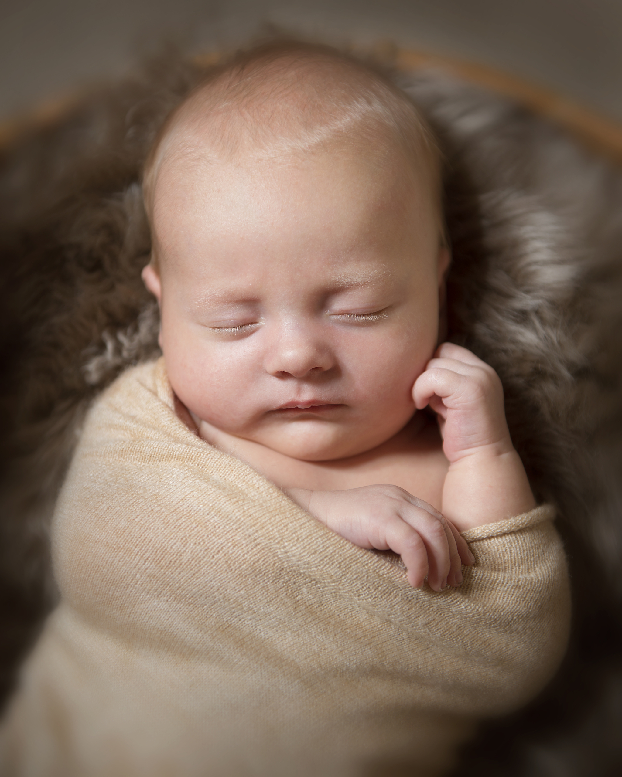 nyfødt ligger på brunt saueskinn med ansiktet mot kamera