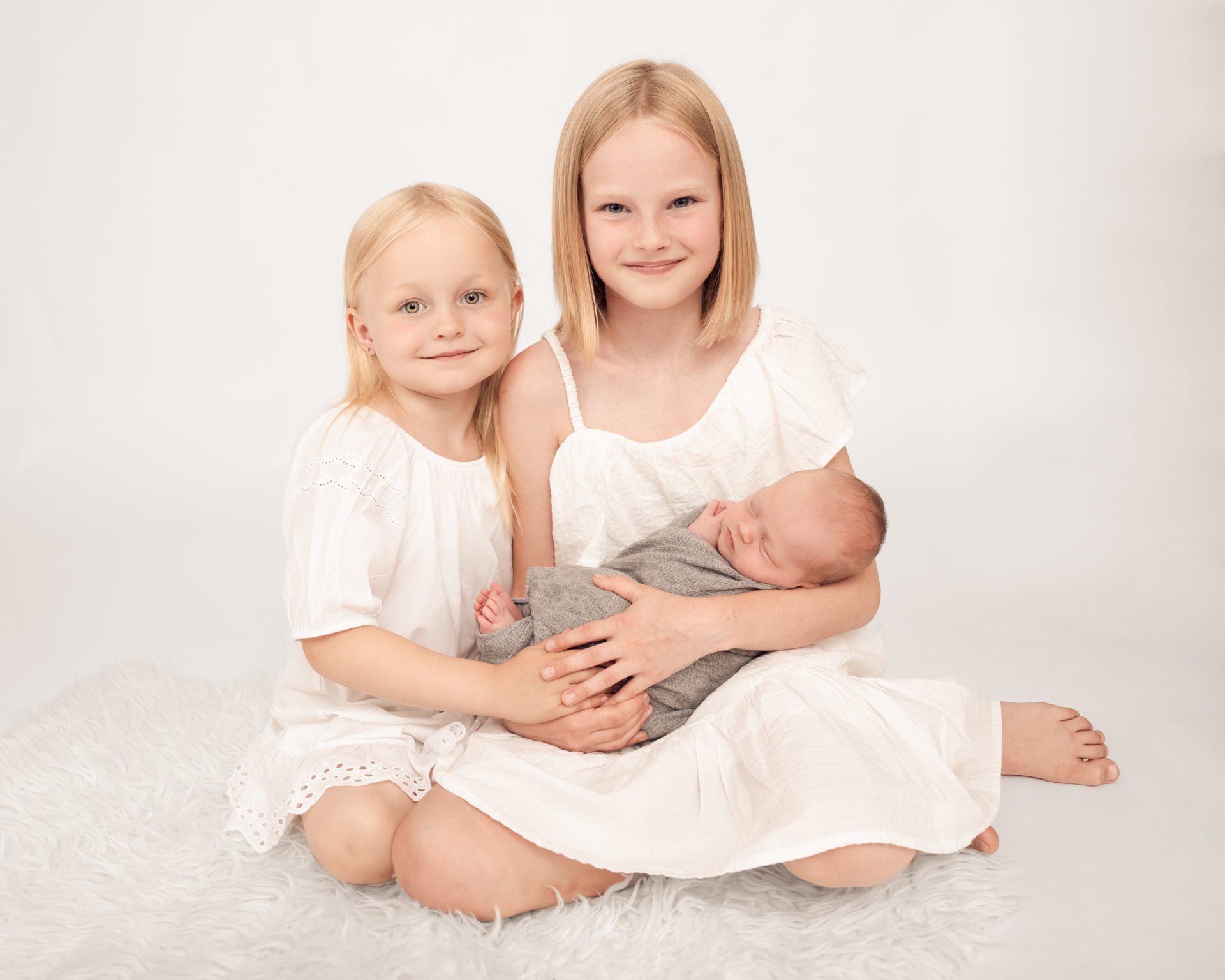 2 søstre holder sin nye lillesøster som kun er noen få dager gammel.