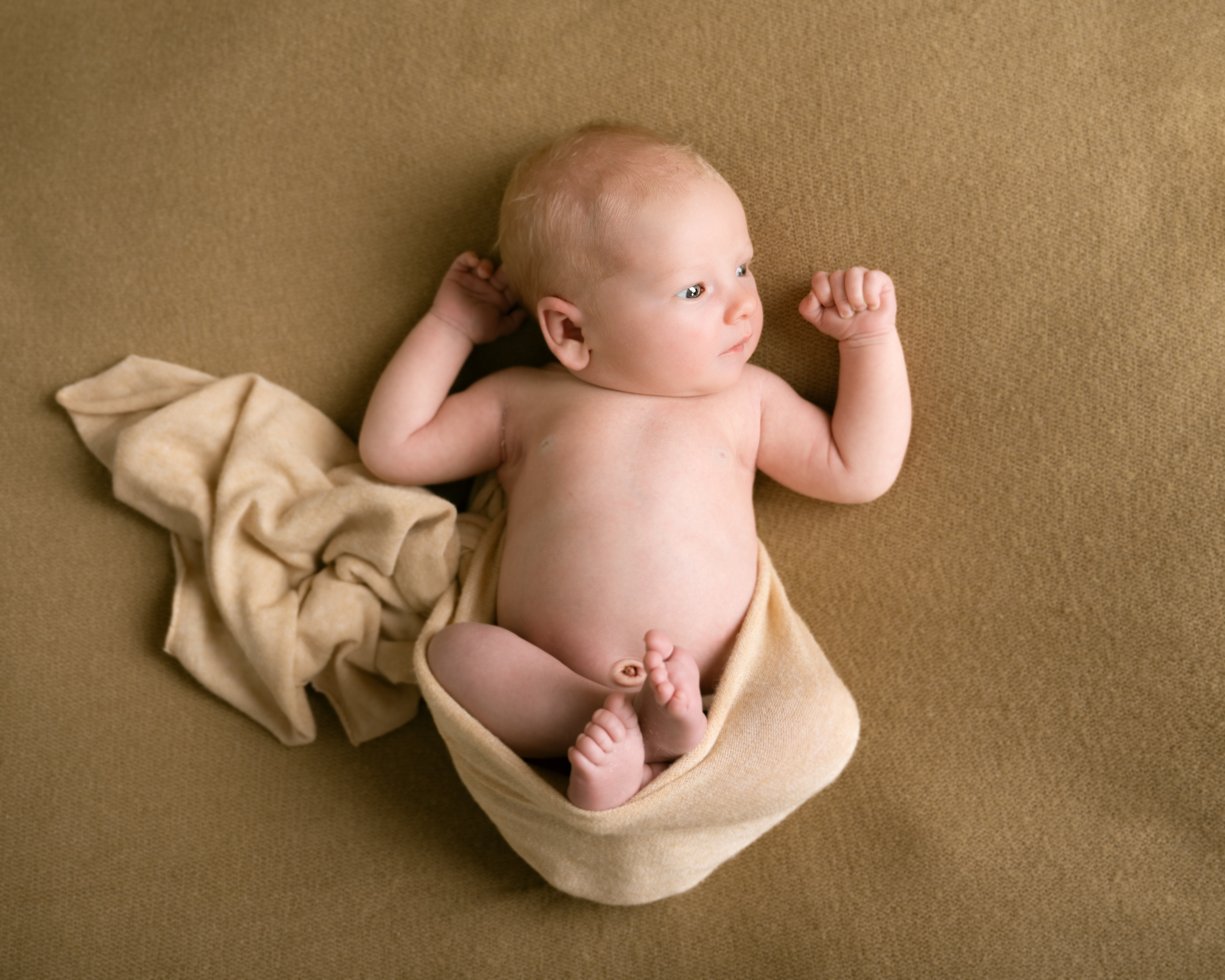 fredfylt liten nyfødt ligger på ryggen intullet i beige stoff.